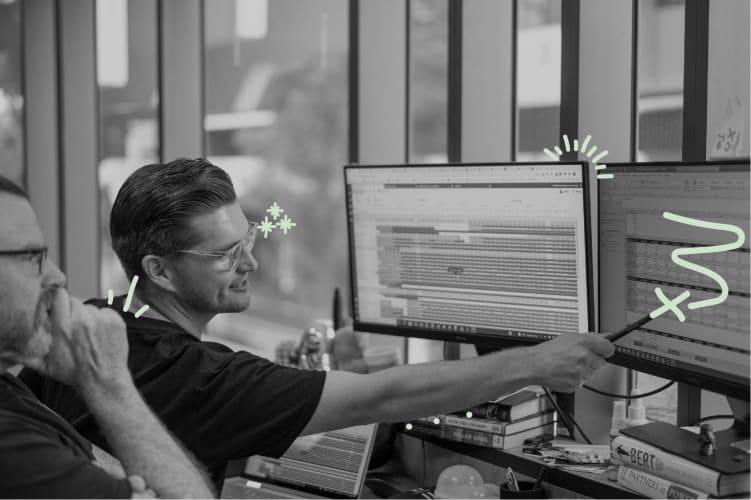 A photo of two men in front of a computer and pointing to the screen
