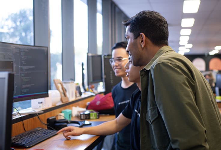 A photo of three men looking at a computer screen