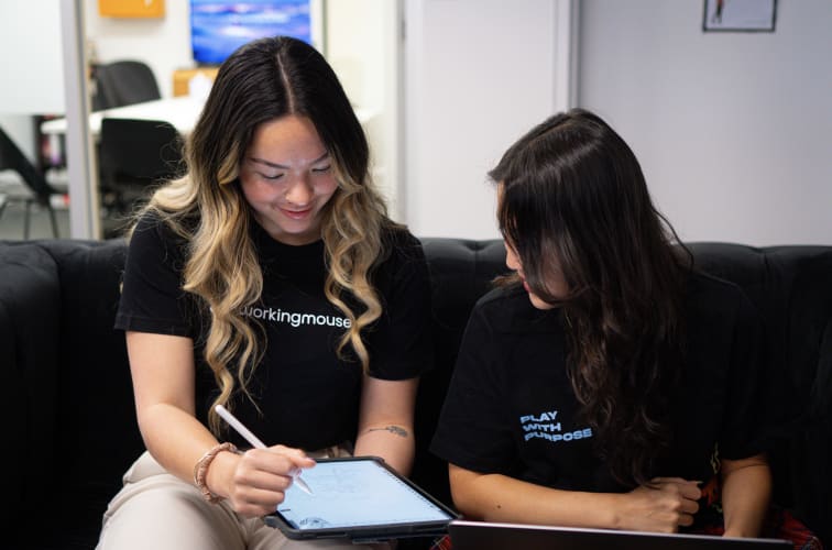 Two women sitting on a couch working on an ipad