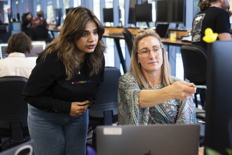 A photo of to women looking at a computer screen, one is pointing to the screen