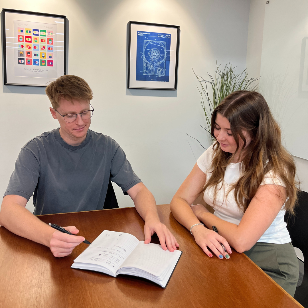 A man and a woman sitting at a desk looking at a notebook