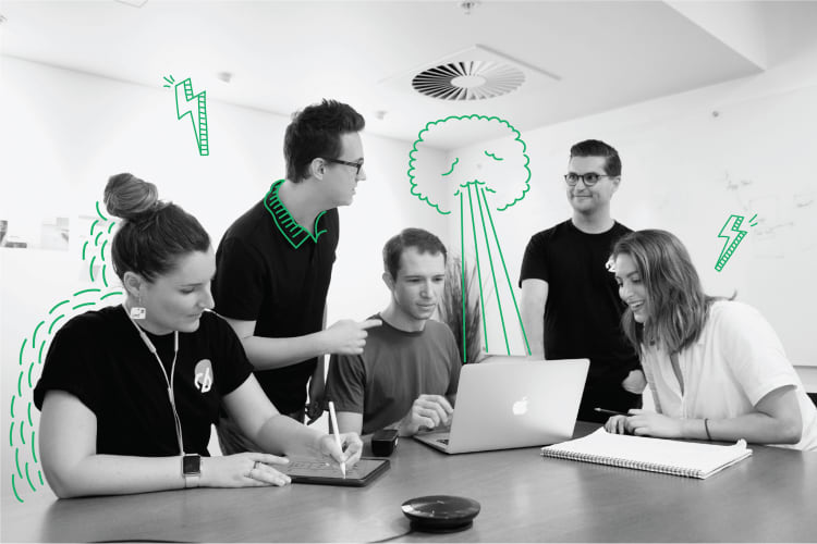 A black and white photo of 5 people aorund a desk. They are using llapops and ipads. There is green doodles on the phoo (lightening bolts and lines)