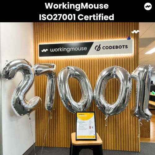 WorkingMouse celebrates achieving ISO 27001 certification with silver balloons spelling ‘27001’ in front of the WorkingMouse and Codebots signage. The image highlights the company’s compliance with international information security management standards, showcasing the certification document in a festive setting